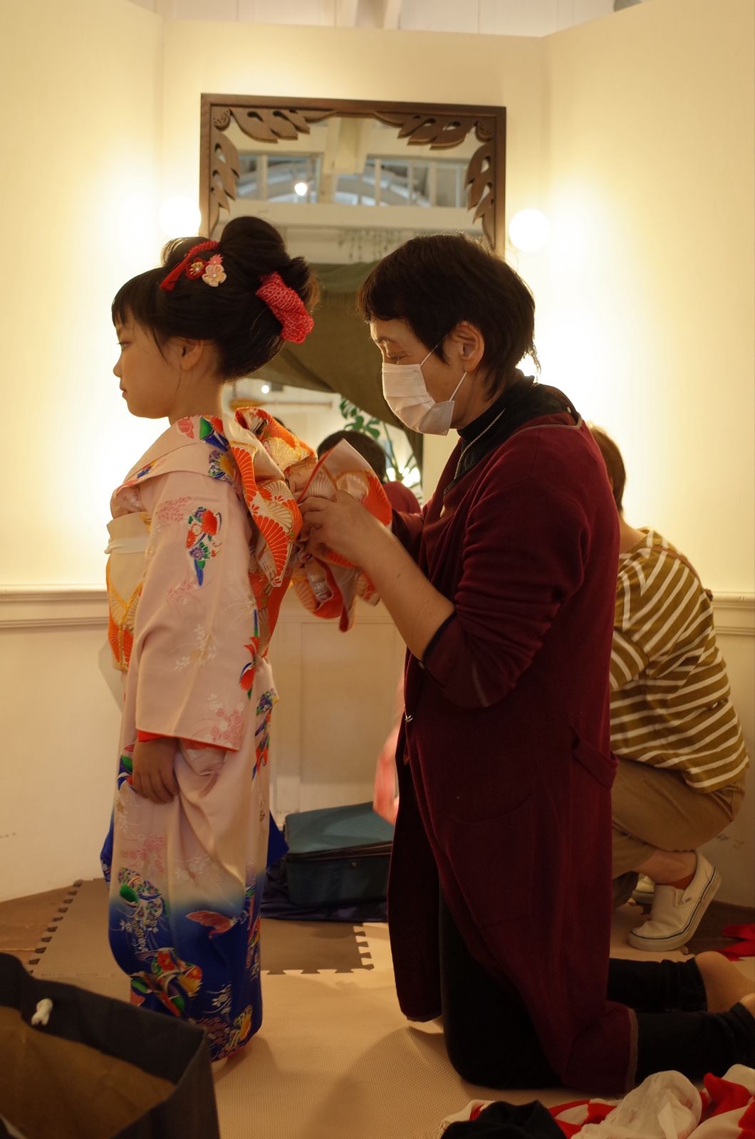 ハリウッドミラーの前で帯を結んでもらう女の子
