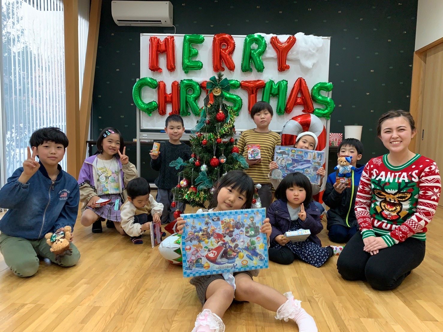 クリスマスツリーの前でプレゼントを持つ子どもたちと講師